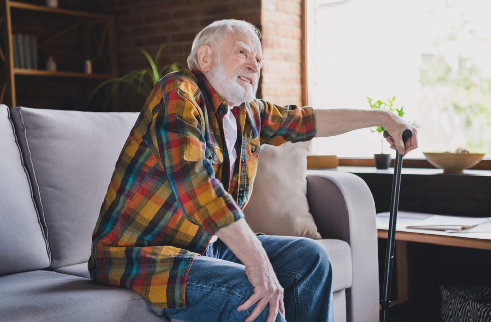 A frustrated senior holds their knee as they struggle to get up from the couch.