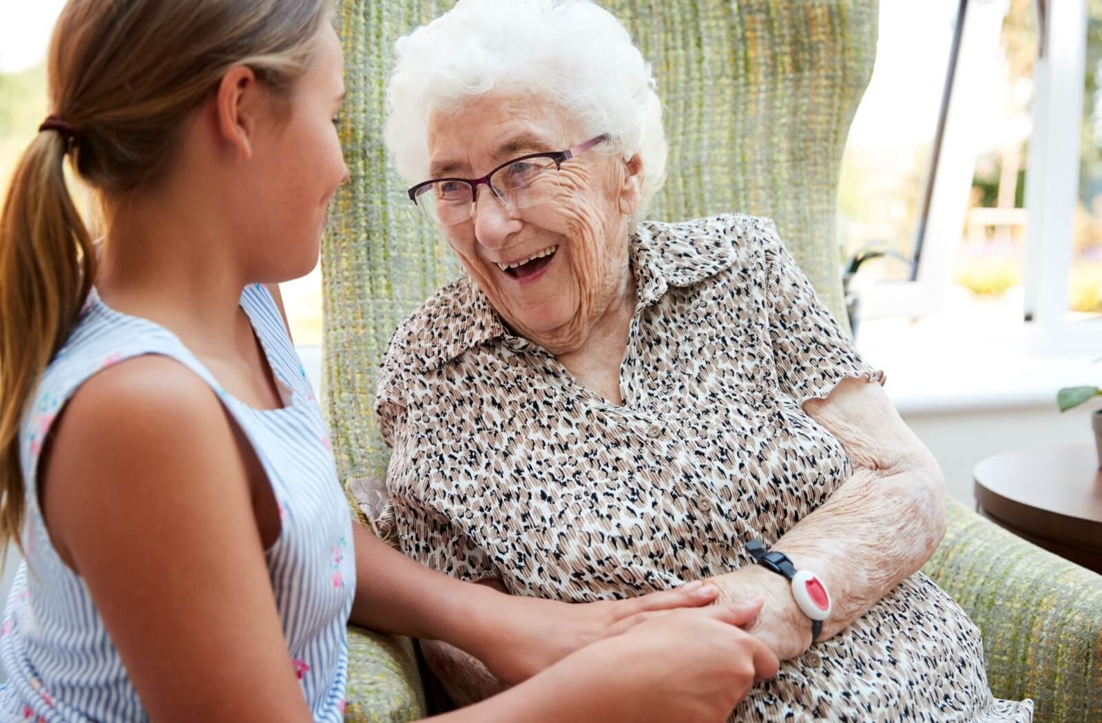 An older adult laughs while clasping their grandchild's hand during a visit in senior living