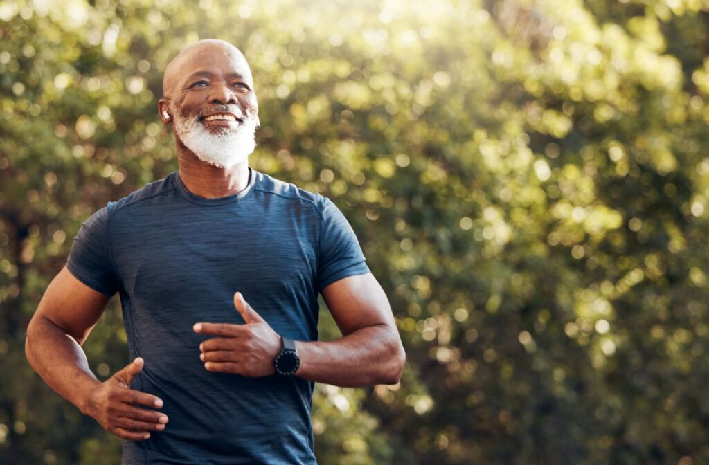 A mature adult in a blue athletic shirt listens to music while running through a local park