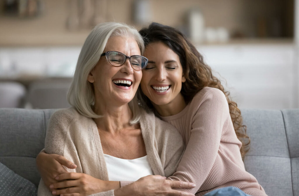 An adult child hugging their senior parent with dementia while they both laugh after a joke.