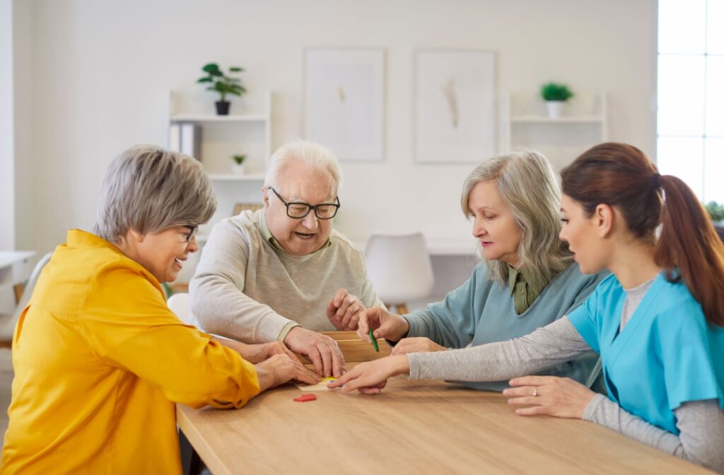 Seniors and caregiver gathered around a table playing a game together in a bright community activity room